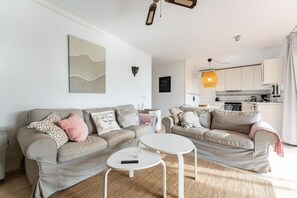 Een moderne woonkamer met twee banken, een witte salontafel en een keuken op de achtergrond.