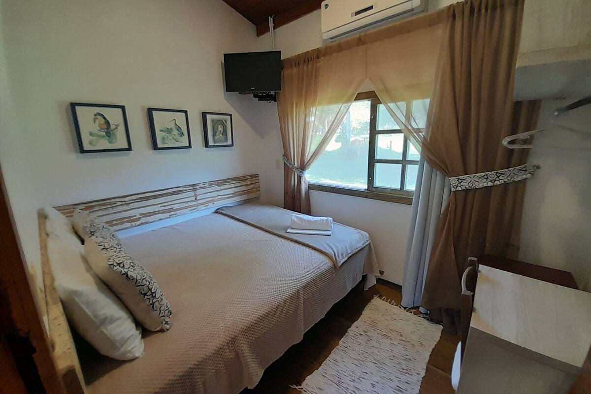 A bedroom with a bed, a window with curtains, a mounted TV, and framed pictures on the wall.