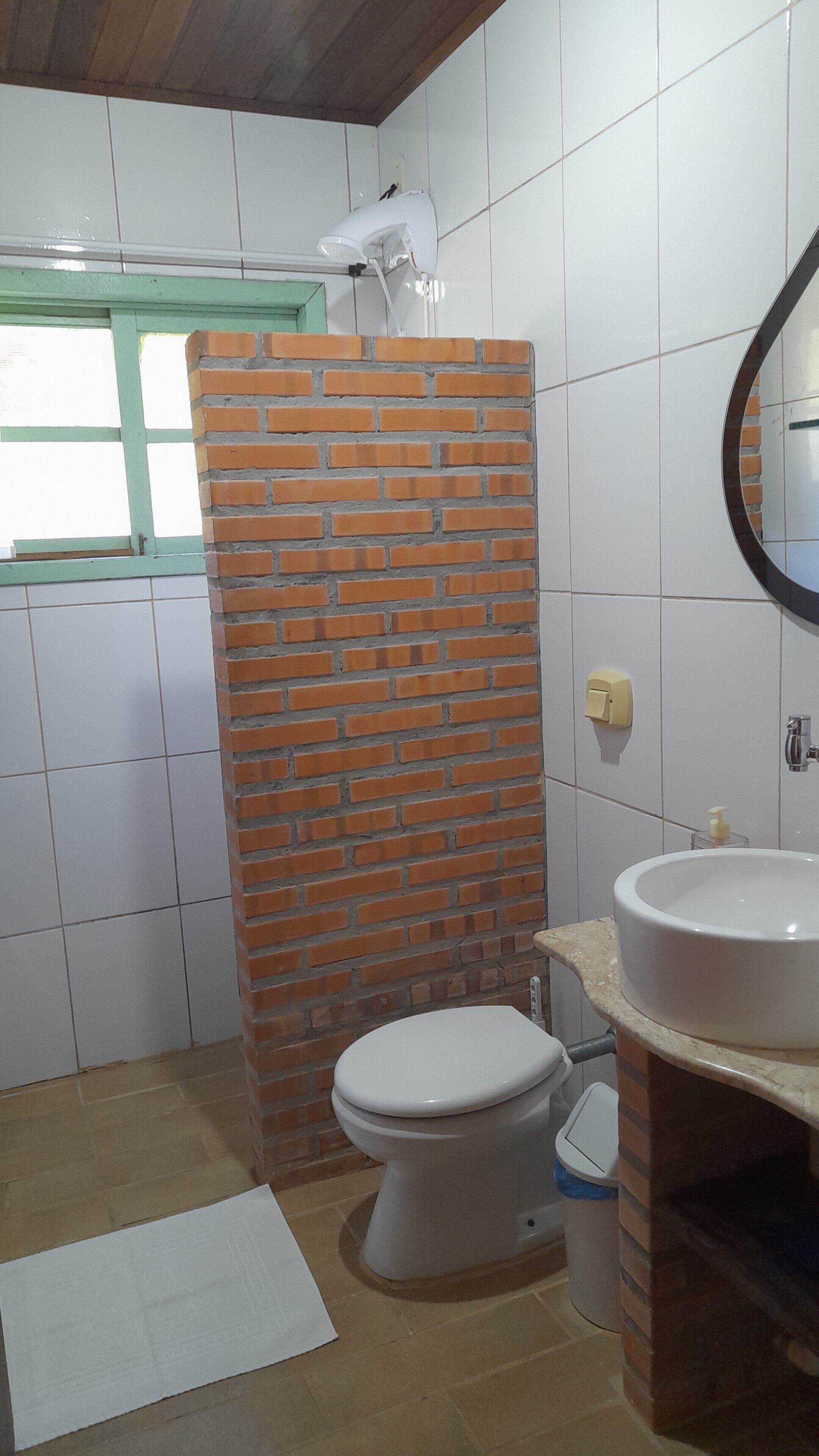 Un baño con inodoro, lavamanos y zona de ducha con pared de ladrillo.
