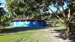 A blue house with a tiled roof, surrounded by a grassy area and trees. - Pousada Sítio Bicho do Mato  (Tijucas)
