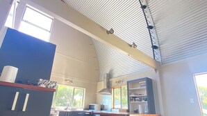 A spacious kitchen with a curved ceiling, a central island with bar stools, and a view of the outdoors through large windows.