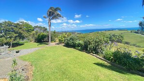 A lush garden with a palm tree, a white fence, and a view of the sea.
