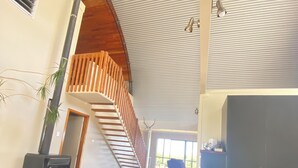 A modern interior with a long wooden table, a staircase with wooden railings, and a large window providing natural light.