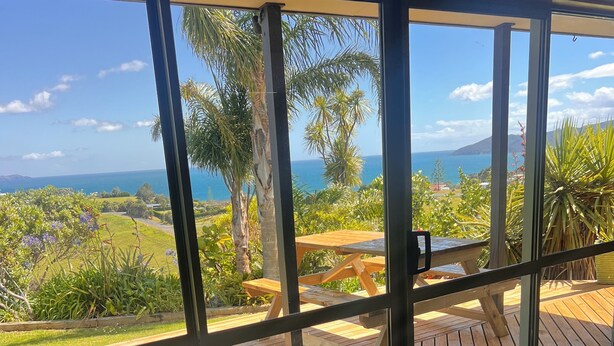 A balcony with a wooden deck, a glass door, and a view of the ocean and greenery.