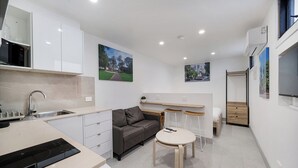 A compact kitchen with a built-in oven, a sink, and a dining area with a small table and stools. There is a sofa and a TV in the living area. - Cosy Studio (Redfern)