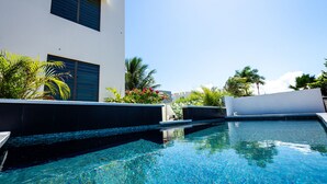 A clear blue pool with a modern building in the background, surrounded by tropical plants. - Luxury Cliffside Oceanview Villa with Private Pool and Rooftop. Accommodates 7. (Isabela)
