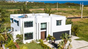 A modern two-story house with a flat roof, large windows, and a well-maintained lawn. - Luxury Cliffside Oceanview Villa with Private Pool and Rooftop. Accommodates 7. (Isabela)
