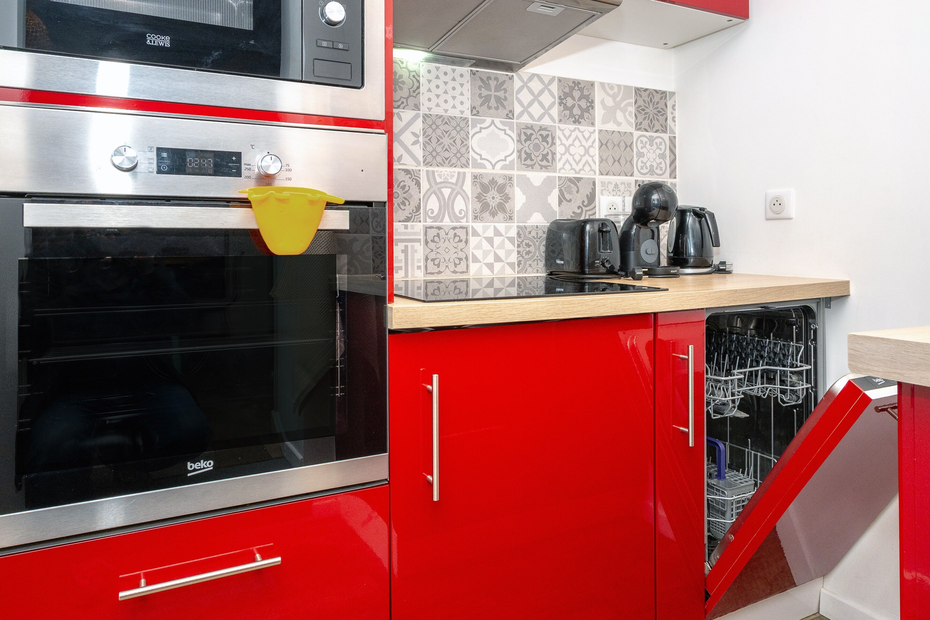 A kitchen with a red cabinet, a black oven, a coffee maker, and a dishwasher.