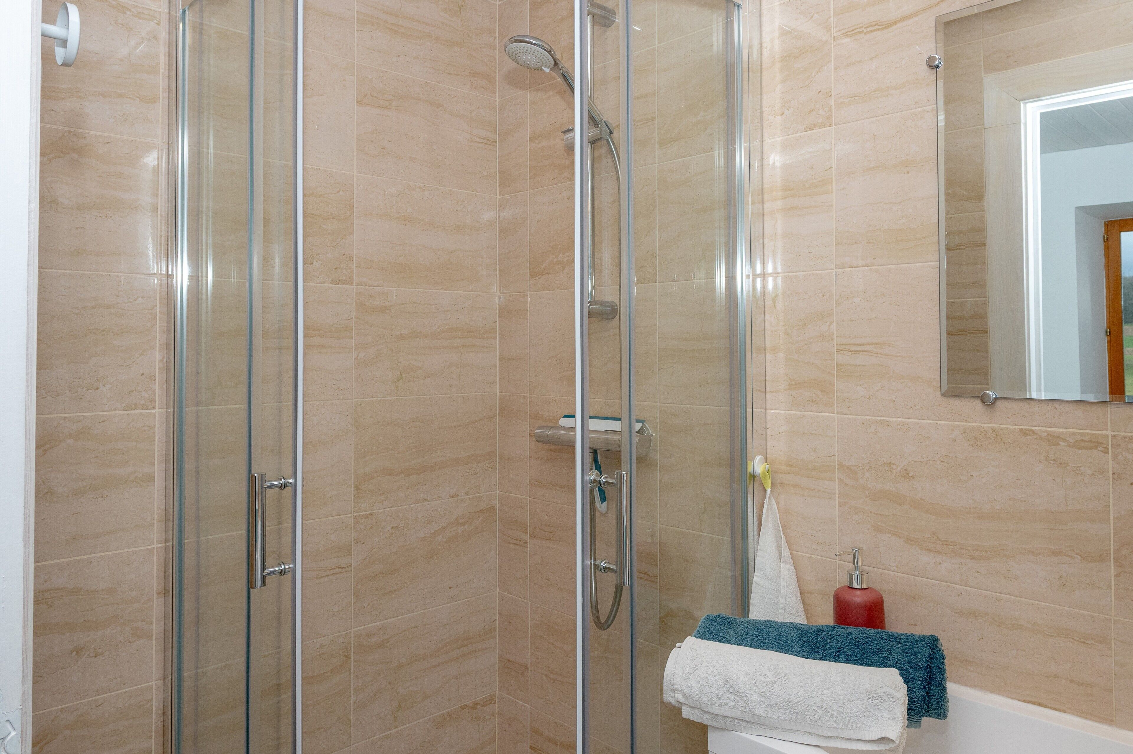 A glass-enclosed shower area with a handheld showerhead and a wall-mounted faucet.