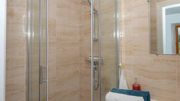 A glass-enclosed shower area with a handheld showerhead and a wall-mounted faucet.