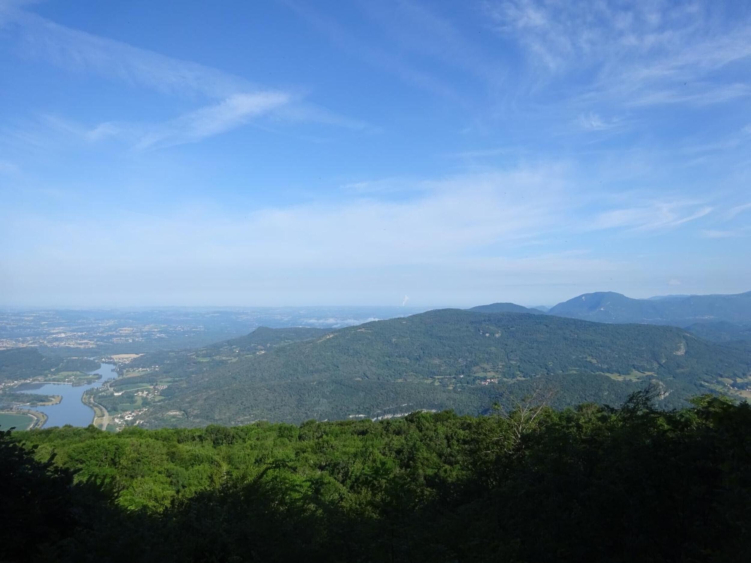 Paesaggio montuoso con fitta foresta, un fiume e colline in lontananza.