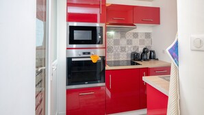 Eine kleine Küche mit roten Schränken, einer Mikrowelle, einem Backofen und einer Kaffeemaschine.