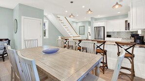 Une cuisine moderne avec des meubles blancs, une table à manger en bois et un escalier menant à un autre niveau.