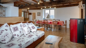 Un espacio acogedor con techo de madera, un sofá con cojines estampados, una mesa de comedor con sillas y un refrigerador rojo y negro.