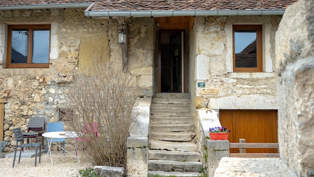 Un edificio de piedra con puerta de madera, un pequeño porche con mesa y sillas, y una escalera que conduce a la entrada.