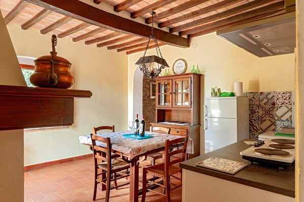 A kitchen with a dining table, chairs, a hanging light fixture, a cabinet, and a refrigerator.