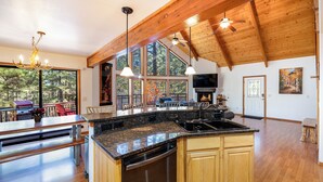 Une cuisine spacieuse dotée d’un grand îlot central, de poutres en bois et offrant une vue sur l’extérieur.