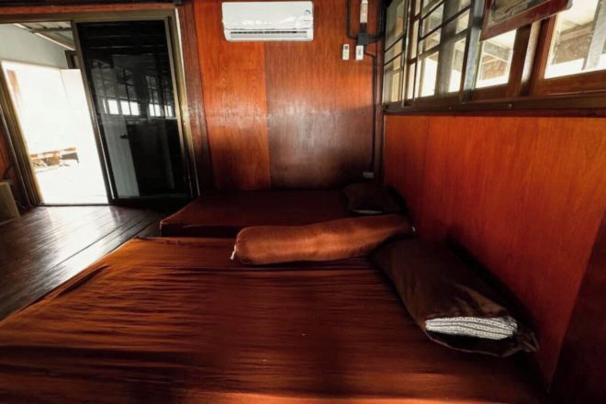 A room with a wooden floor, a bed with a headboard, and a window with a view.