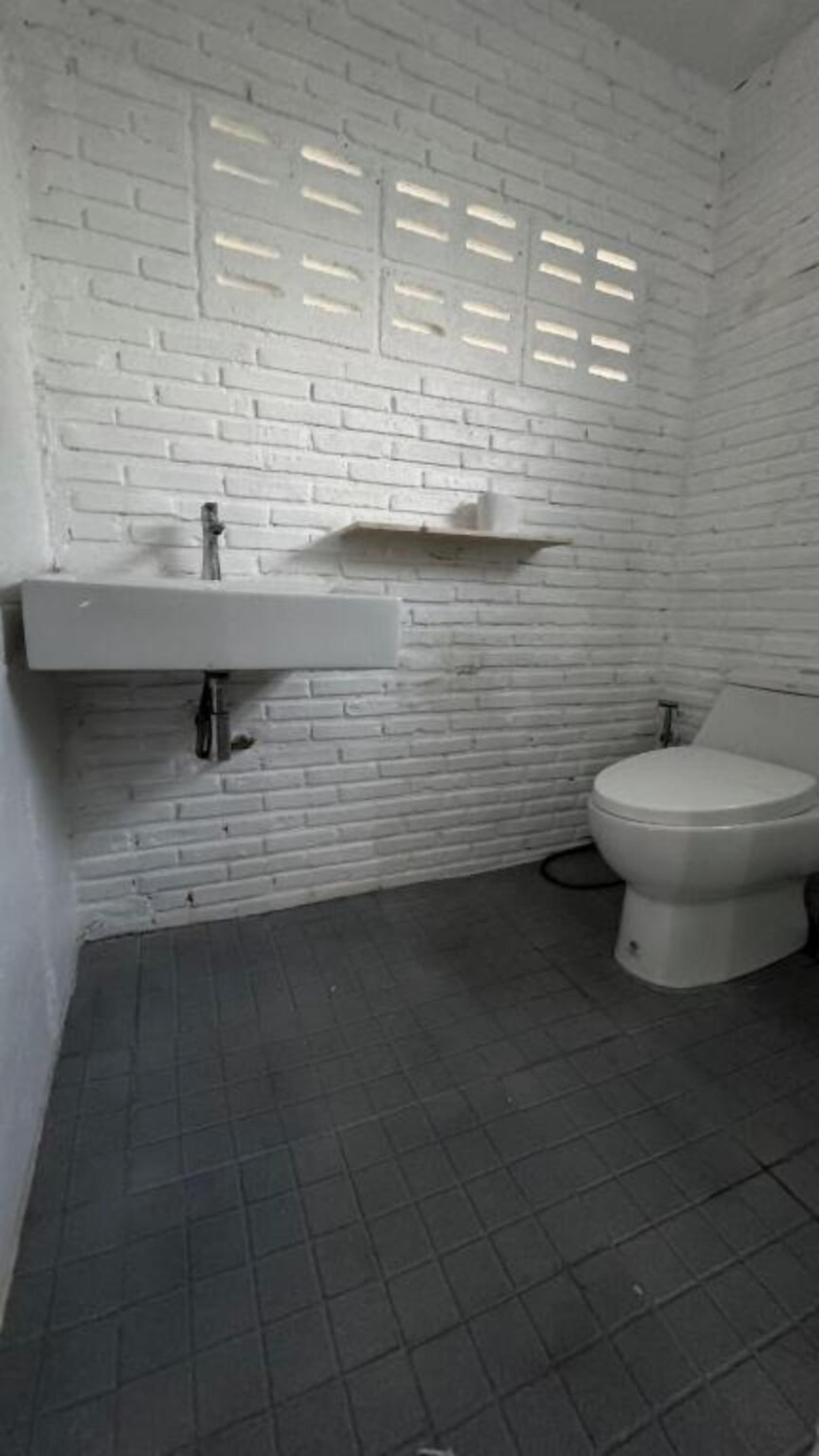Un baño con pared de ladrillo blanco, lavamanos blanco y un inodoro.