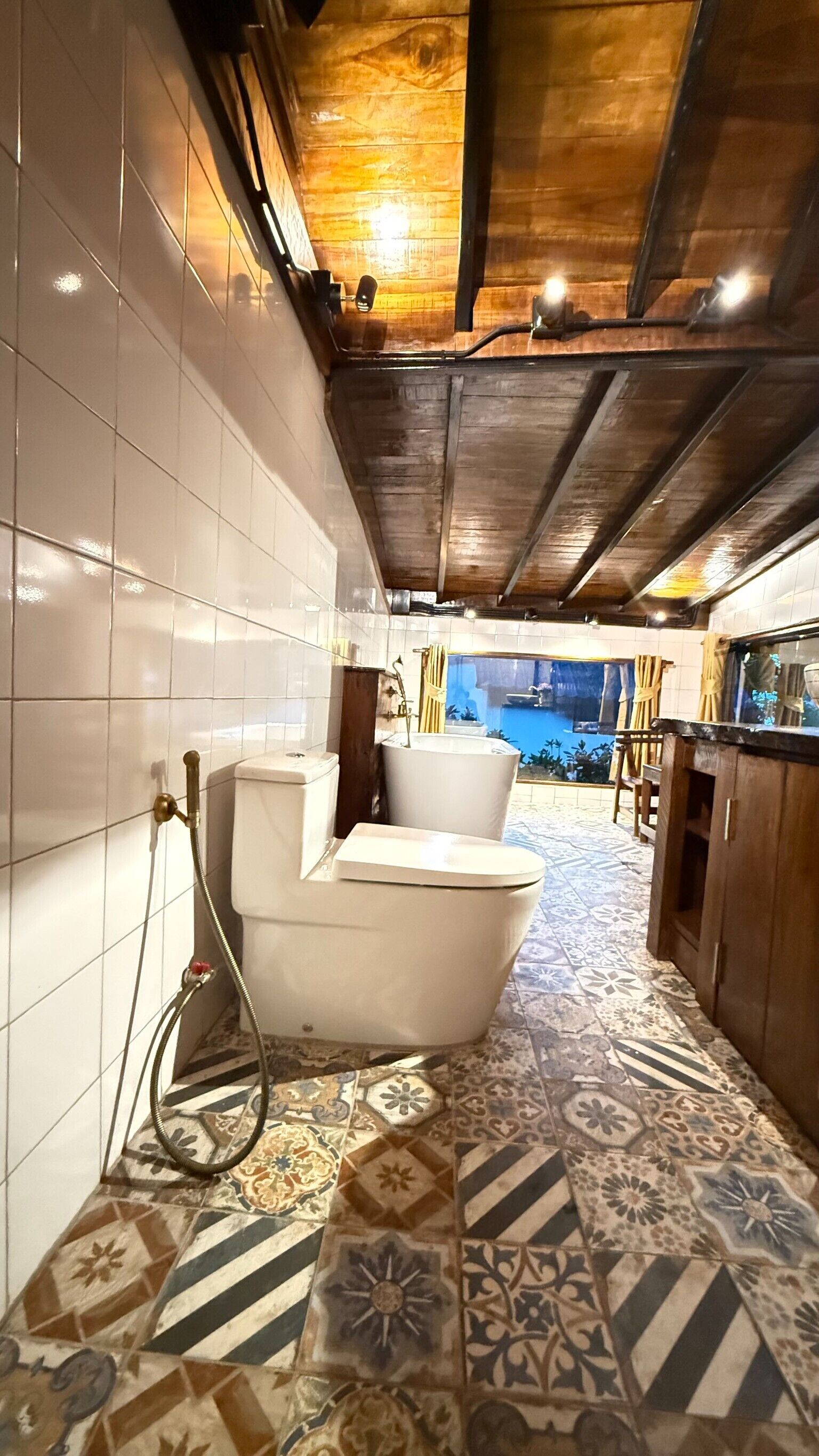 A bathroom with a bathtub, shower, and toilet. The floor has patterned tiles, and the ceiling has exposed wooden beams.
