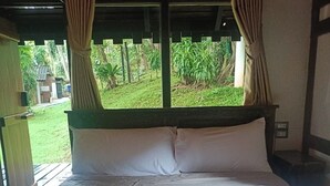 A bed with white linens and a pet bed, curtains, and a view of greenery outside.