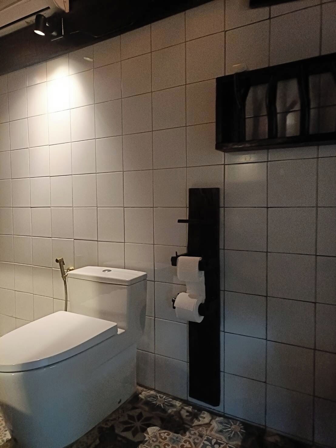 A bathroom with white tiled walls, a toilet, a shower, and a toilet paper holder.
