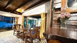 A wooden bar area with a table and chairs, a vase of flowers, and a view of a pool through a glass door.