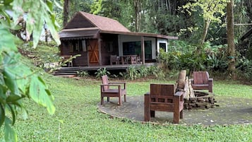 A rustic wooden house with a porch, surrounded by lush greenery.