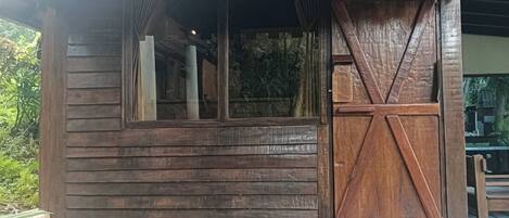 Una baita in legno con tetto spiovente, un'ampia finestra e una porta in legno.