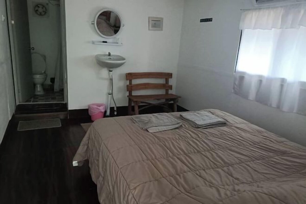 A bedroom with a bed, a wooden chair, a sink, and a mirror.