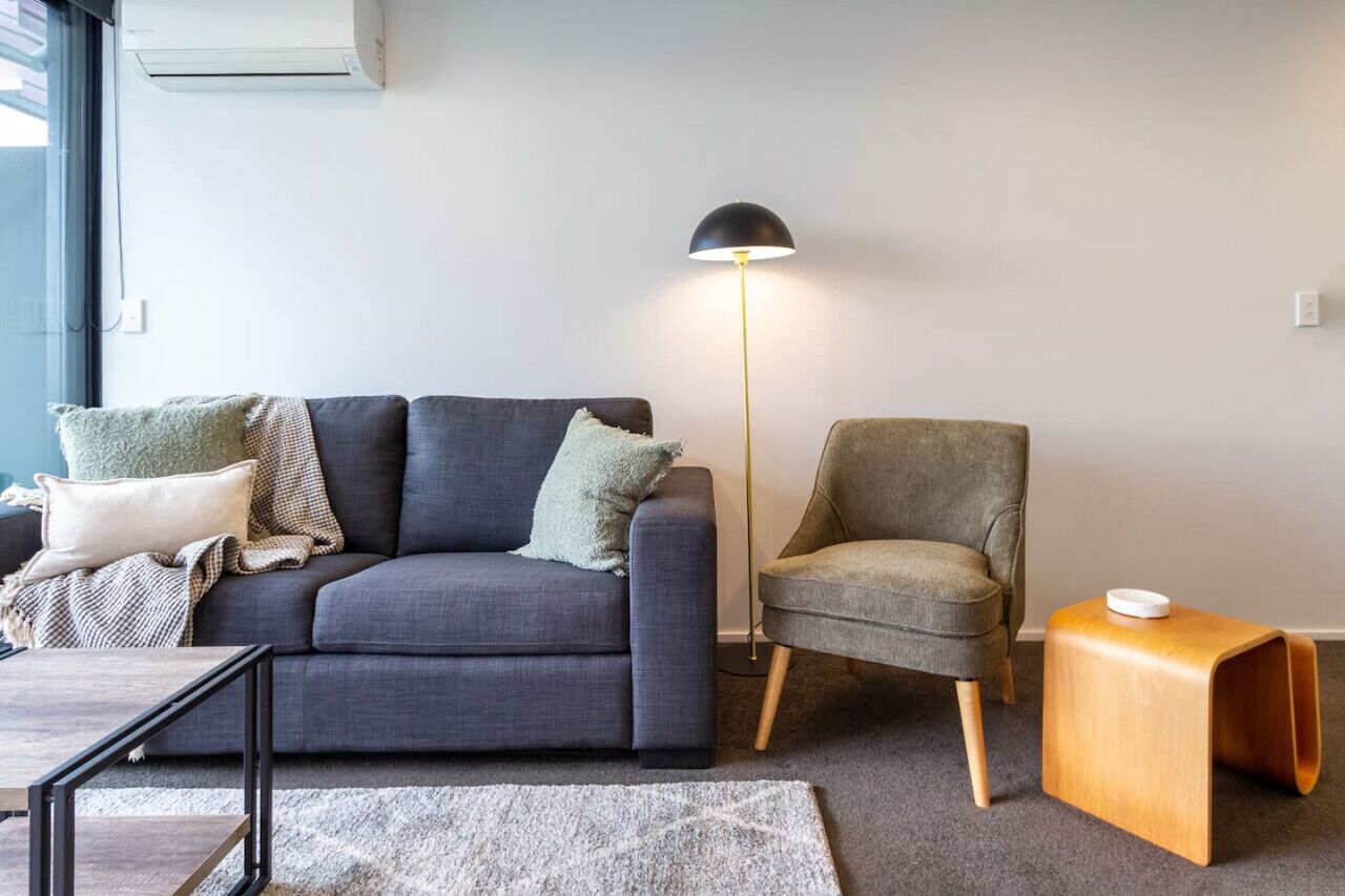 A modern living room with a grey sofa, a grey armchair, a wooden side table, and a floor lamp.