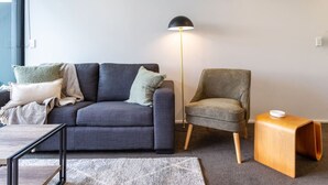 A modern living room with a grey sofa, a grey armchair, a wooden side table, and a floor lamp. - Dashing 2-Bedroom Apartment in Vibrant City Hub (Christchurch)