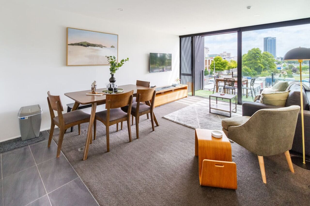 A modern living room with a dining area, large windows, and a view of the city.