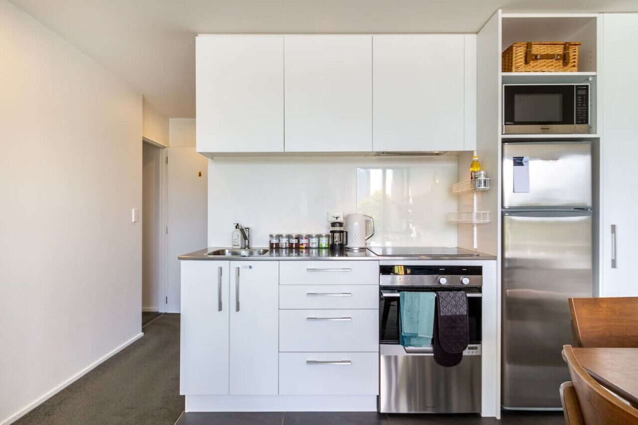 A compact kitchen with white cabinets, a stainless steel oven, and a microwave.