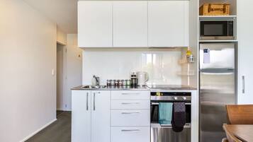 A compact kitchen with white cabinets, a stainless steel oven, and a microwave.