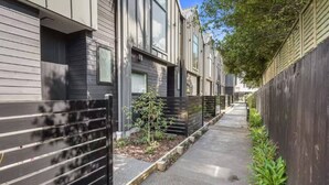Un moderno edificio residencial con un sendero estrecho, cercas de metal y pequeñas plantas.
