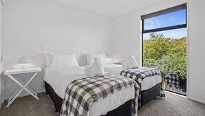 Un dormitorio moderno con dos camas, una mesita pequeña y un ventanal con vistas a zonas verdes.