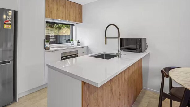 Una cocina moderna con armarios blancos, un revestimiento de pared de madera, un refrigerador de acero inoxidable, un microondas y un fregadero.