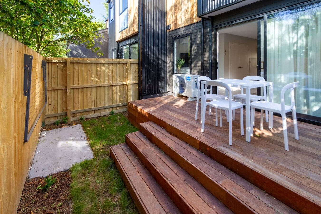 Una terraza de madera con mobiliario exterior y un ventanal corredera que da a una habitación.