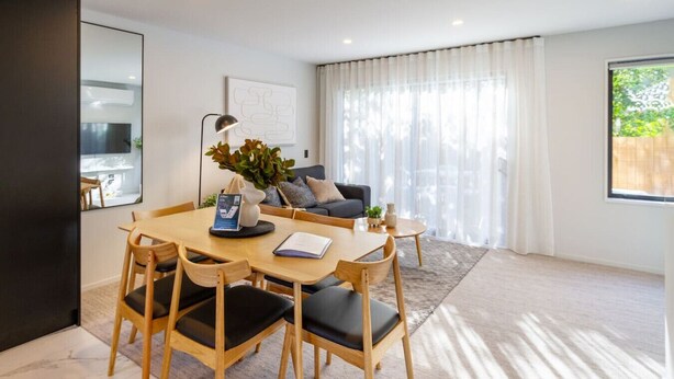 A modern living room with a dining area, featuring a wooden table and chairs, a sofa, and a large window with sheer curtains. - 2 bed 2 bath with Carpark near Canterbury University (Christchurch)