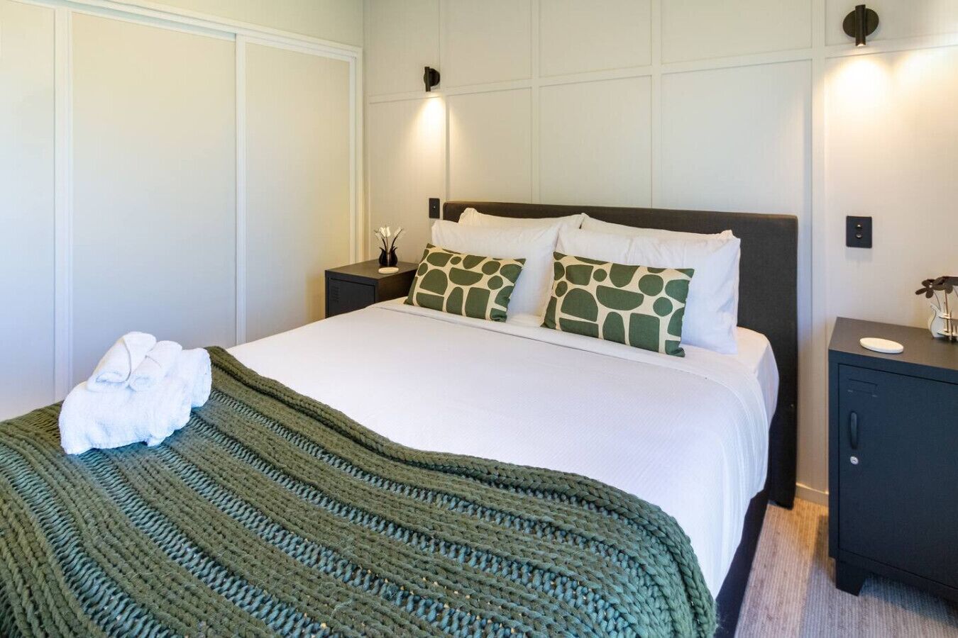 A neatly made bed with a green striped blanket, two matching pillows, and a pair of white towels on the side.