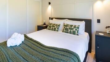 A neatly made bed with a green striped blanket, two matching pillows, and a pair of white towels on the side.
