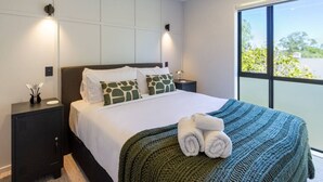 A modern hotel room with a large bed, two bedside tables, a wardrobe, and a view of greenery through a large window. - Walk to Canterbury Uni has own private car park (Christchurch)