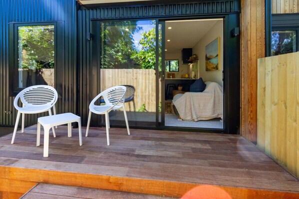 A modern house with a patio area featuring two white plastic chairs and a bench.