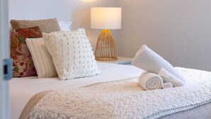 A neatly made bed with white bedding, a rolled towel, and decorative pillows.