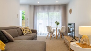 A modern living room with a sofa, a dining table with chairs, a TV, and a lamp.
