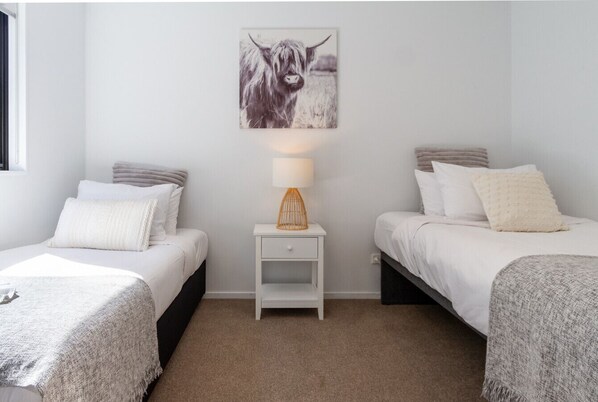 A bedroom with two single beds, a nightstand with a lamp, and a wall-mounted picture of a cow.