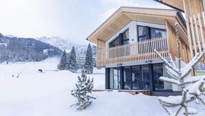 A modern chalet with a wooden balcony, large windows, and a view of a snowy mountain landscape. - Chalet mit 4 Schlafzimmern, Sauna und Kamin (Biberwier)