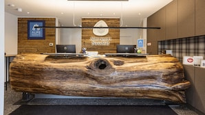 Un comptoir d’accueil avec un grand plateau en bois, deux ordinateurs portables et une enseigne indiquant « Almresort Nassfeld ».