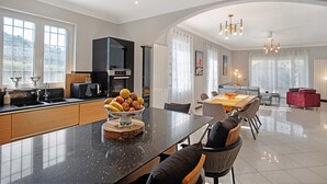 A modern kitchen with a central island, a dining area with a table and chairs, and a living space with a sofa and a red chair.